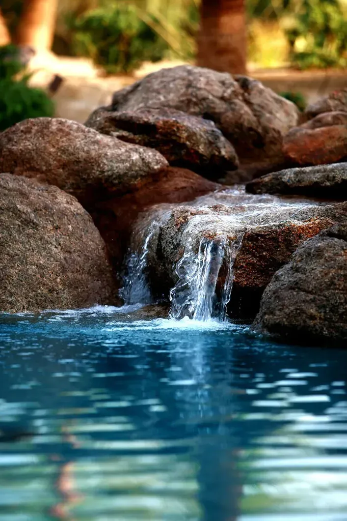 Waterfall cascading into a blue pool, surrounded by brown rocks.