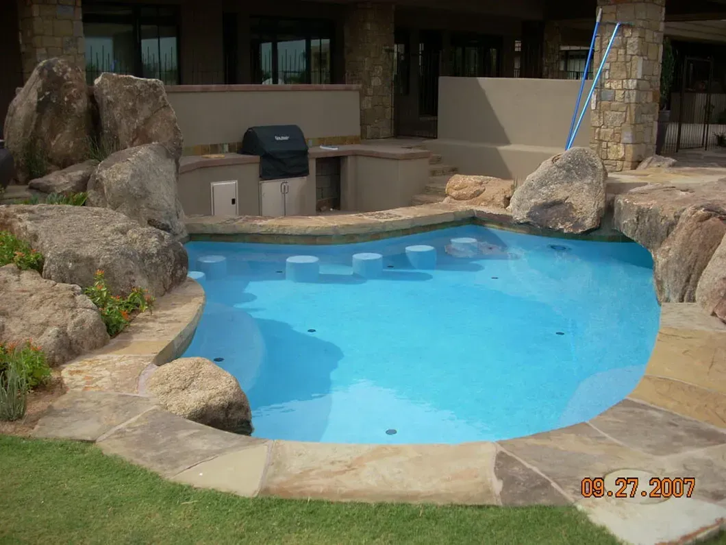 A small, blue-tiled pool surrounded by rocks and a built-in grill area.