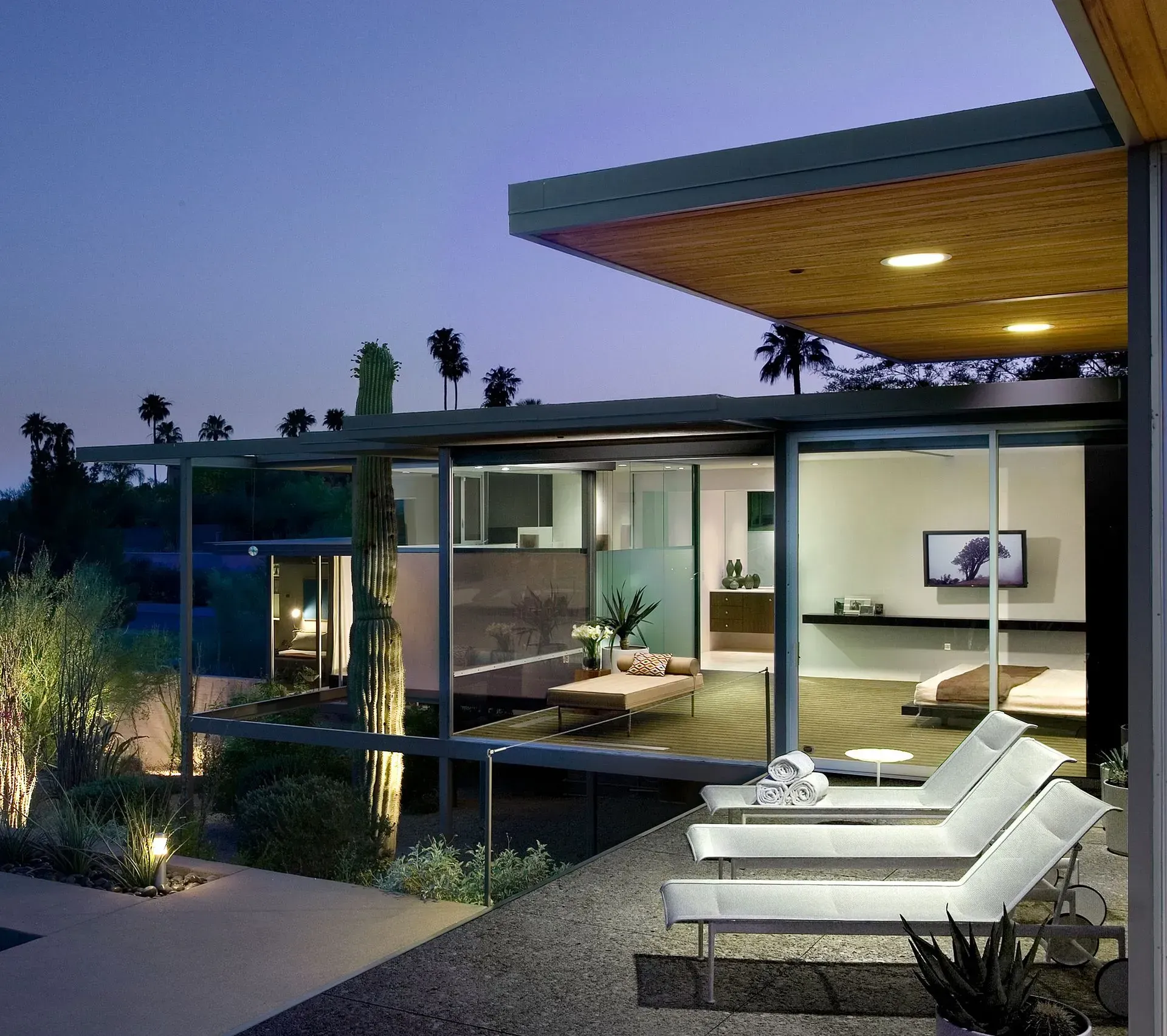 Modern home with glass walls, lounge chairs on patio, and evening sky.