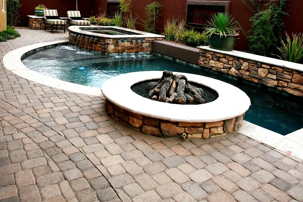 Outdoor patio with pool, spa, and fire pit. Stone pavers, water, and landscaping surround the features.