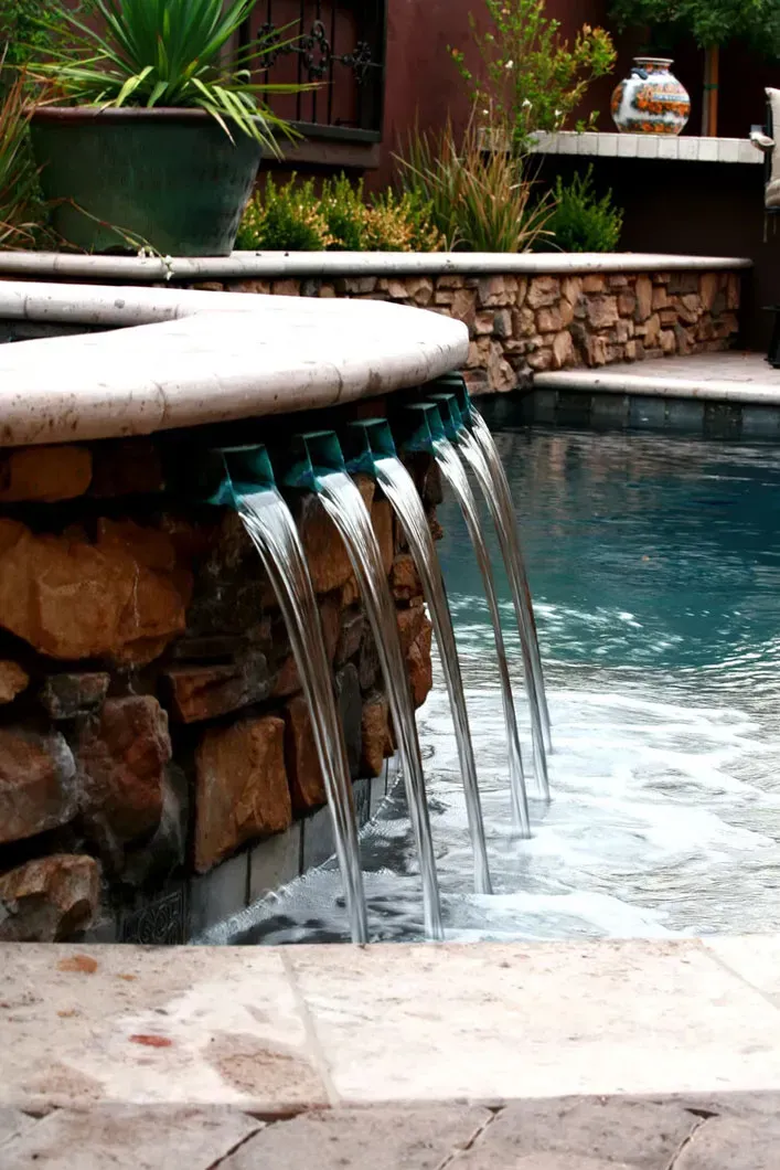 Pool with cascading water feature over a stone wall.