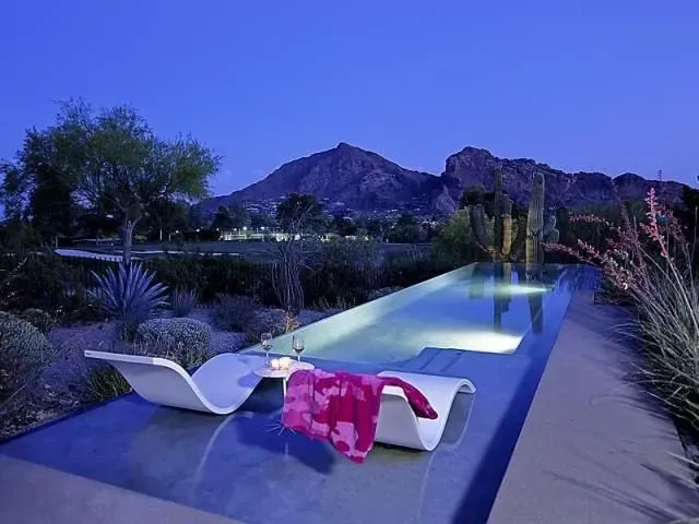 Modern pool with two white chaise lounges, a pink towel, and mountain backdrop at dusk.