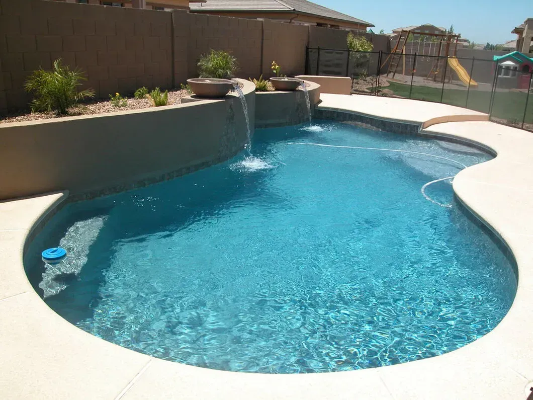 Pool with blue water and a small waterfall in a backyard setting.