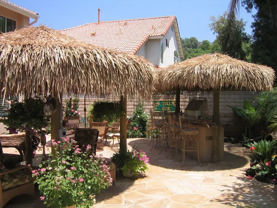 Outdoor tiki bar with thatched roof, stools, and plants on a patio.