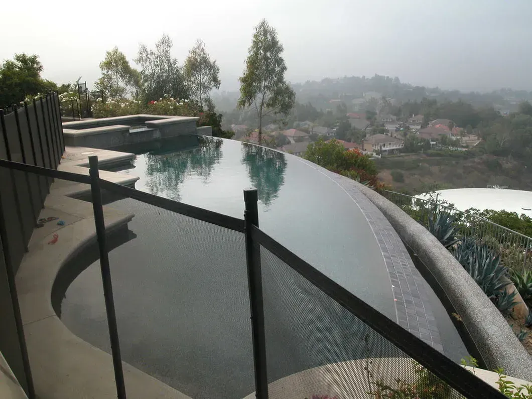 An infinity pool with a view, featuring dark fencing and a hazy landscape in the background.