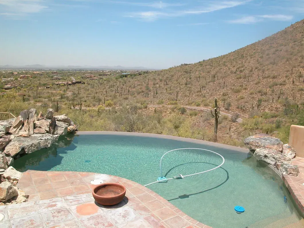 Pool with desert landscape view: turquoise water, terra cotta patio, cacti-covered hills, and clear blue sky.