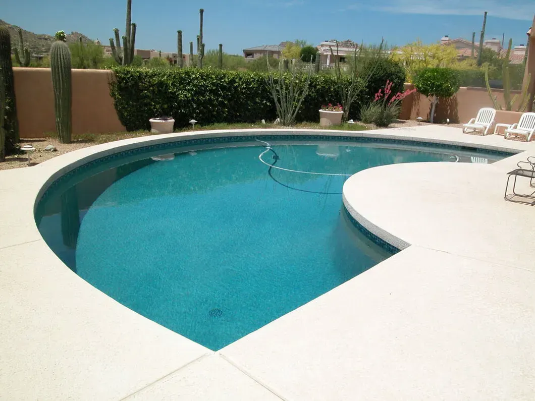 Swimming pool with turquoise water, surrounded by white concrete patio, desert landscape in background.