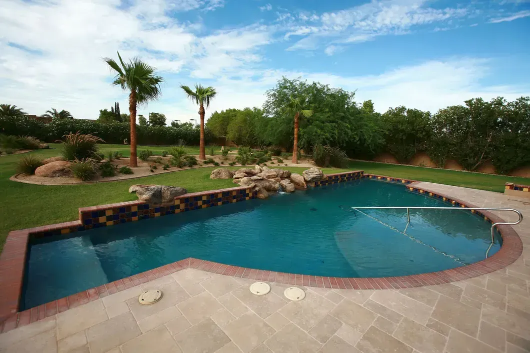 Pool with clear blue water and landscaping, set in a sunny backyard with palm trees.