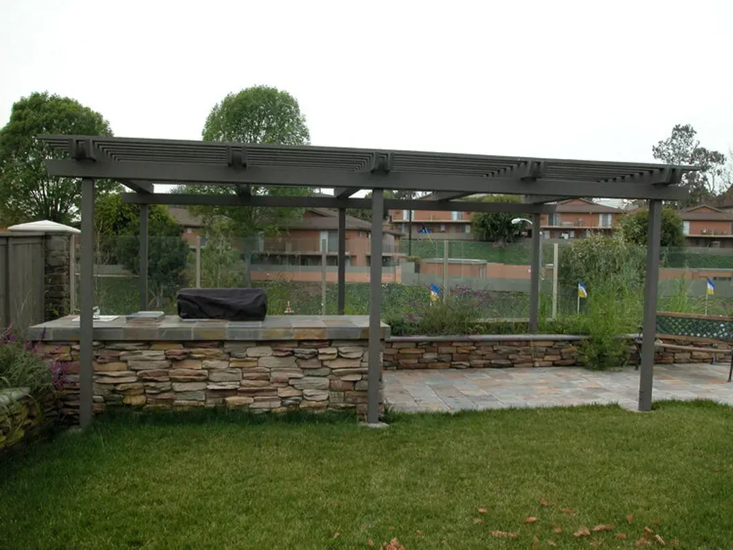 Wooden pergola with stone base, over a grill area and garden.