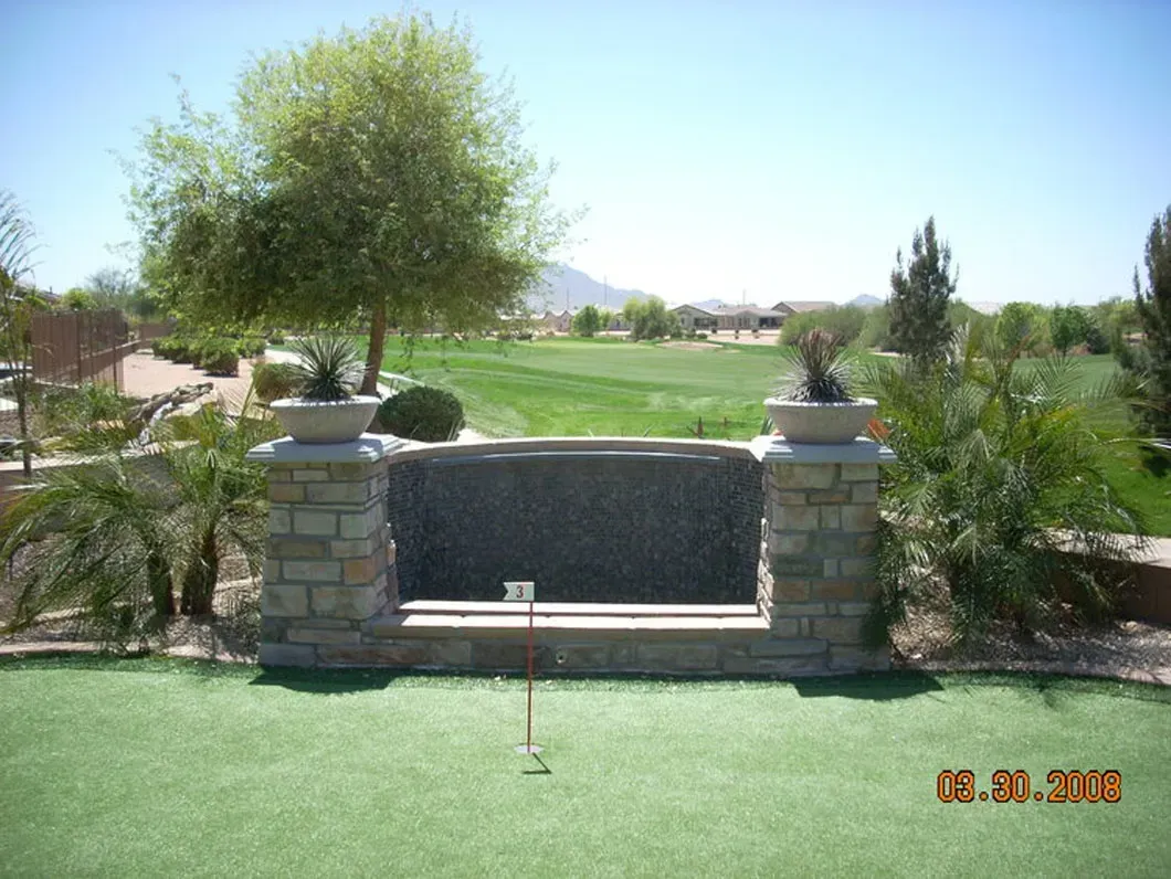 Stone water feature with view of a golf course and greenery under a sunny sky.