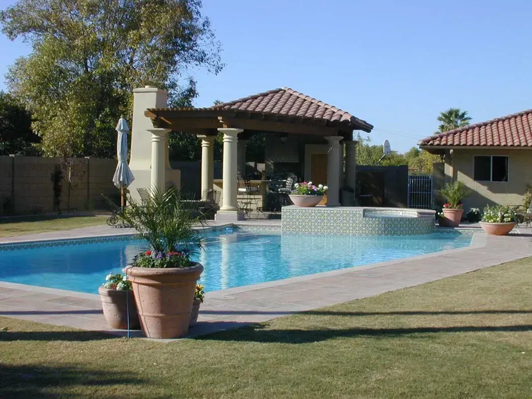 Backyard with a swimming pool, spa, and shaded seating area. Green grass and blue water.