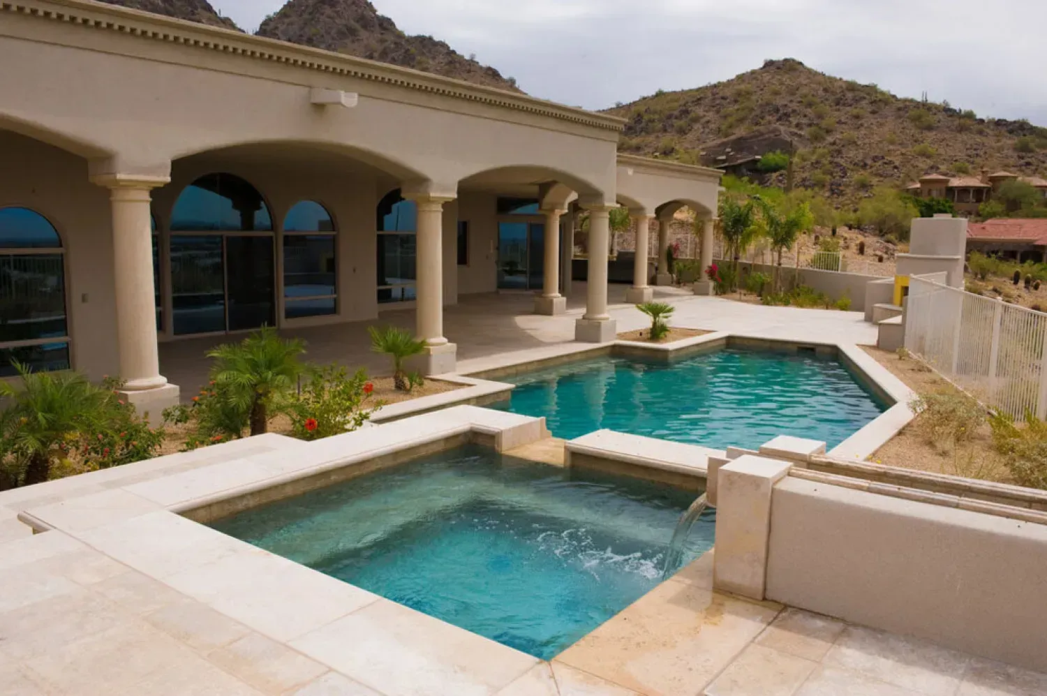 Swimming pool and spa next to a luxury home with desert mountain backdrop.