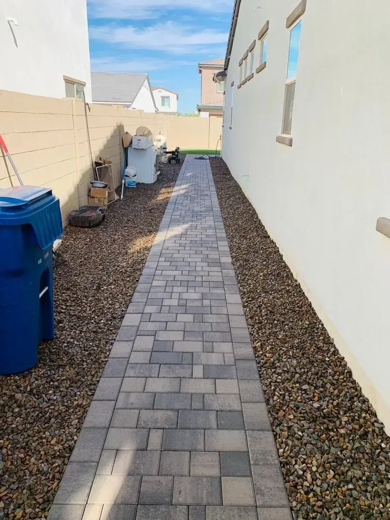A narrow brick pathway with rock beds on either side, between a white wall and a beige wall.
