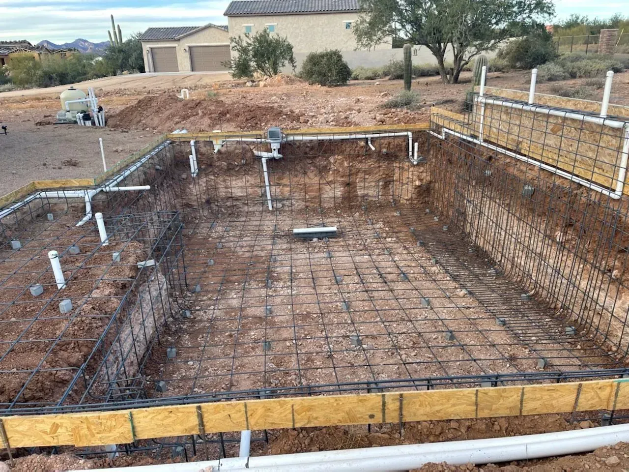 A rectangular pool under construction; dirt walls, steel mesh, white PVC pipes, wooden forms.