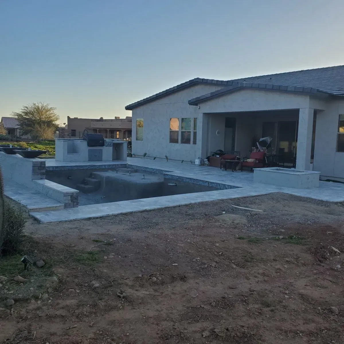Backyard with a swimming pool, patio, outdoor kitchen, and house in a desert setting.
