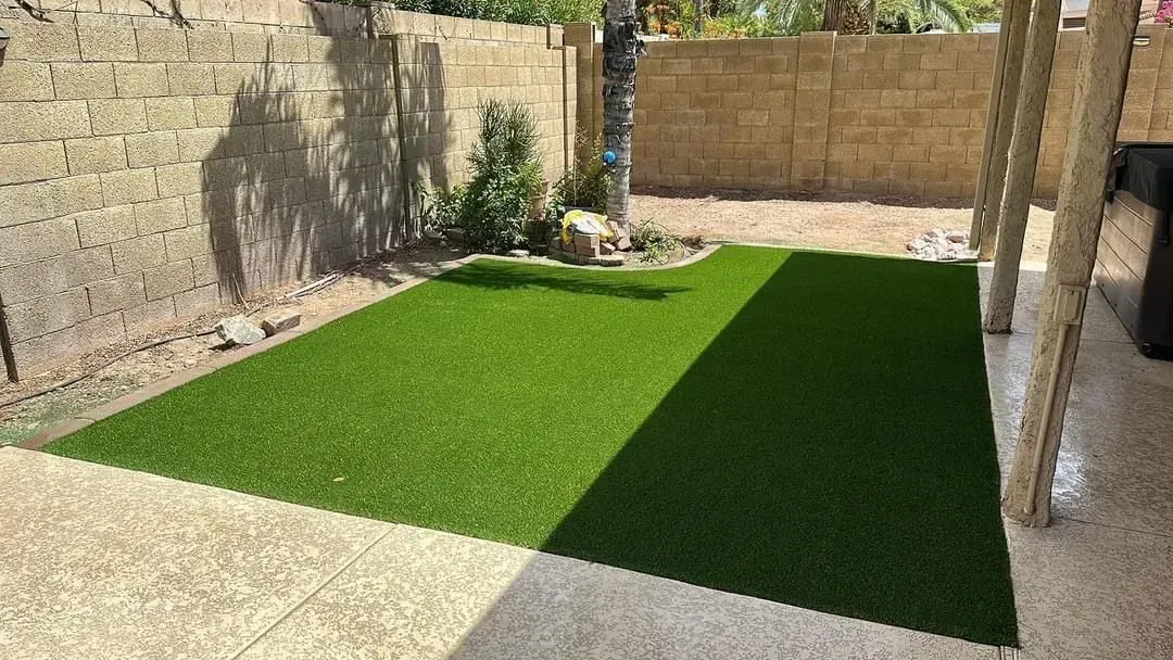 A small backyard with a patch of green artificial turf, surrounded by stone walls and patio.