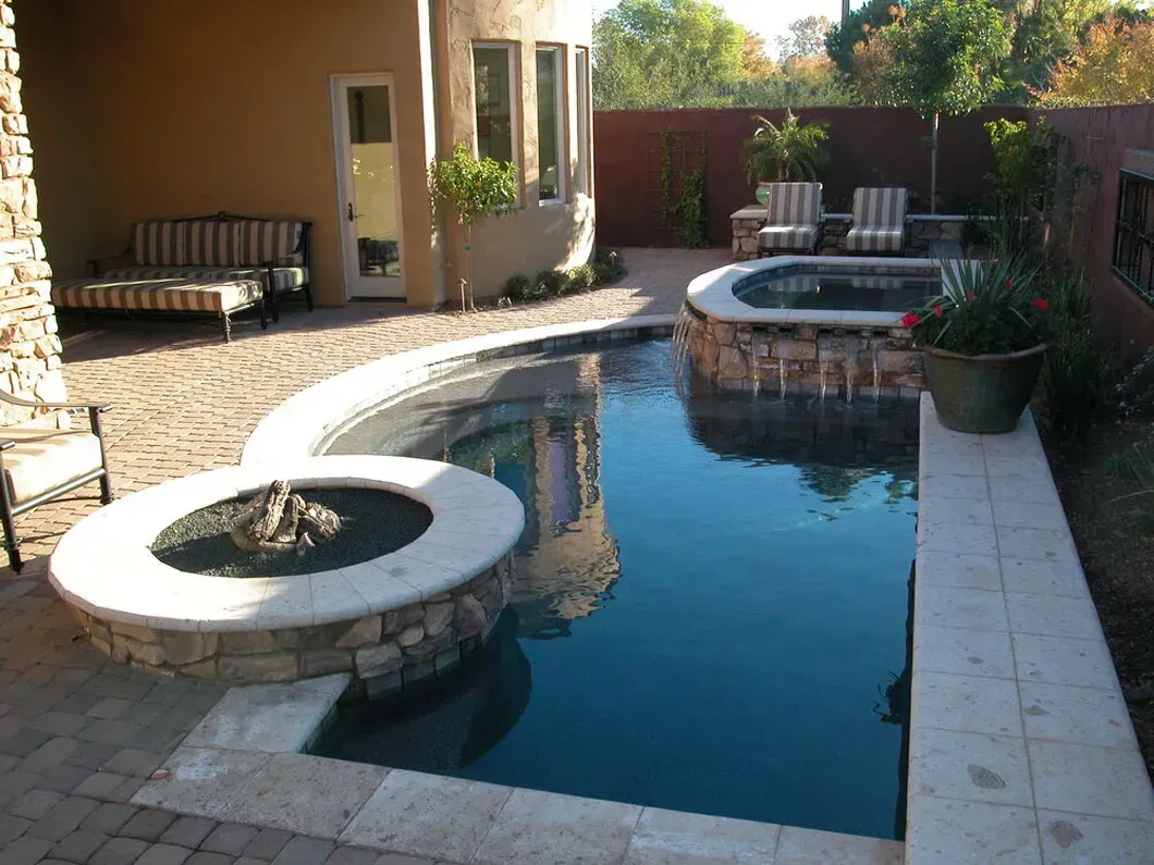 Backyard with a pool, hot tub, and fire pit surrounded by brick and stone, neutral colors.