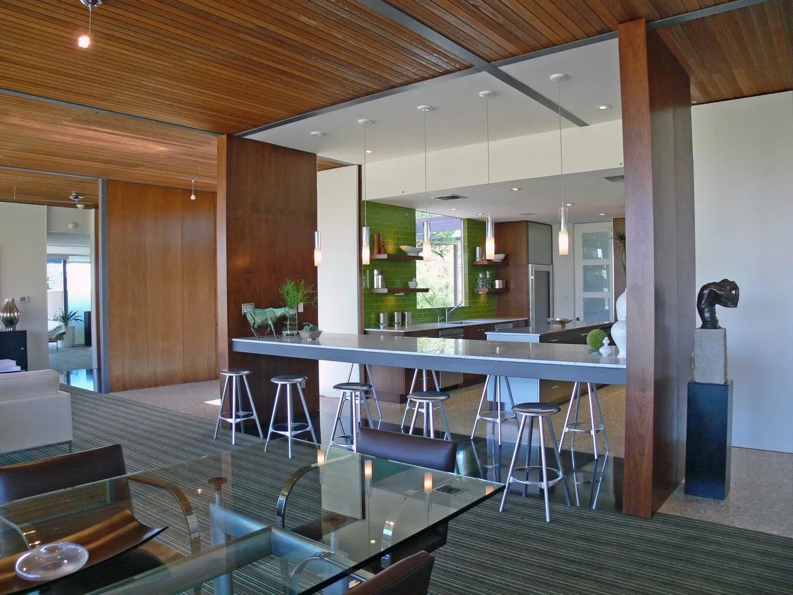 Modern kitchen with dark wood accents, stone countertop, stainless steel stools, and a glass-top dining table.