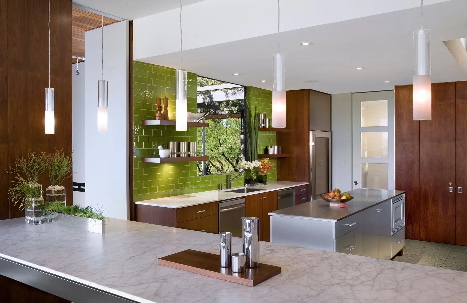 Modern kitchen with green tile backsplash, stainless steel island, and hanging pendant lights.