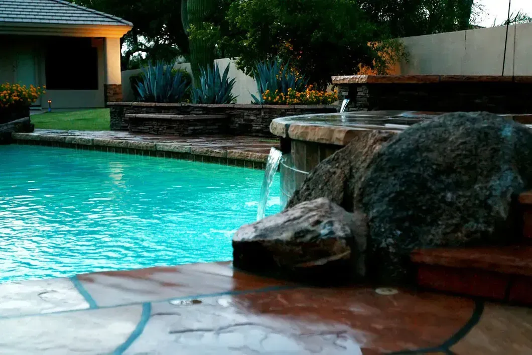 Swimming pool with a rock waterfall feature at dusk.