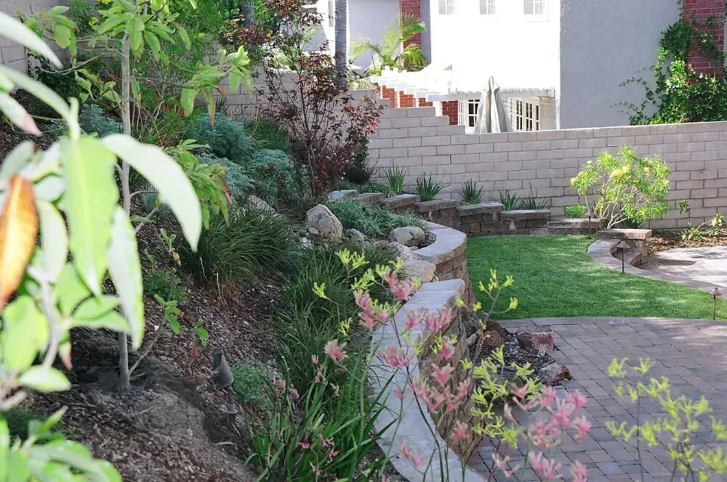 A terraced garden with a stone retaining wall and various plants, near a house.