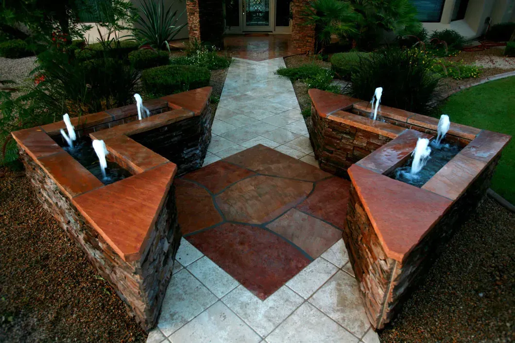 Stone pathway with water fountains on either side, leading to a front door.
