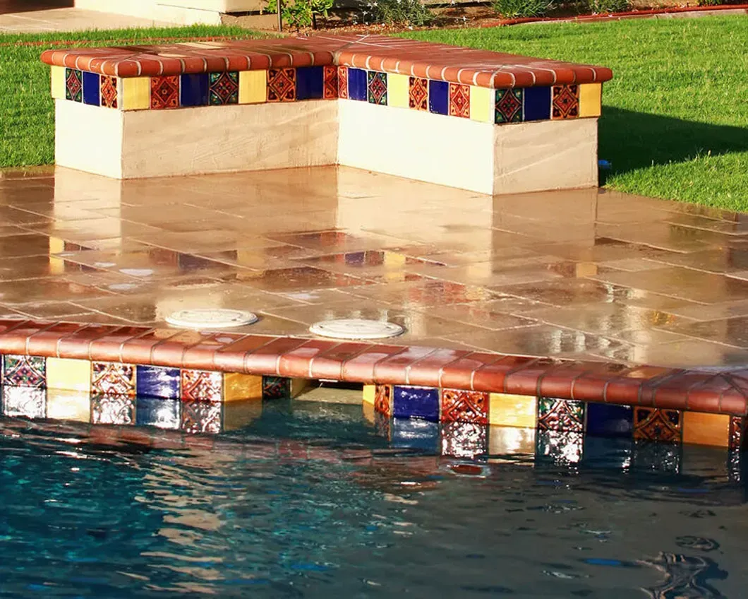 Poolside seating area with decorative tiles, reflecting in wet deck surface.