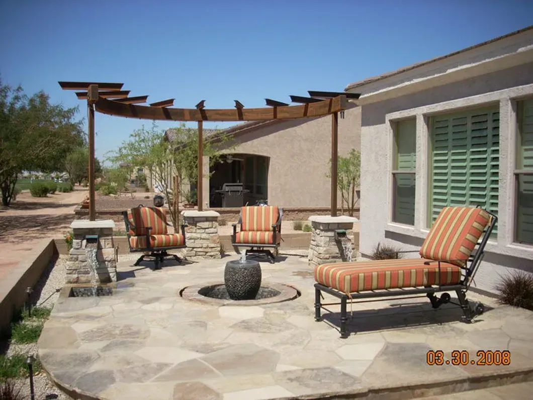 Patio with seating, water fountain, and pergola under a sunny blue sky.