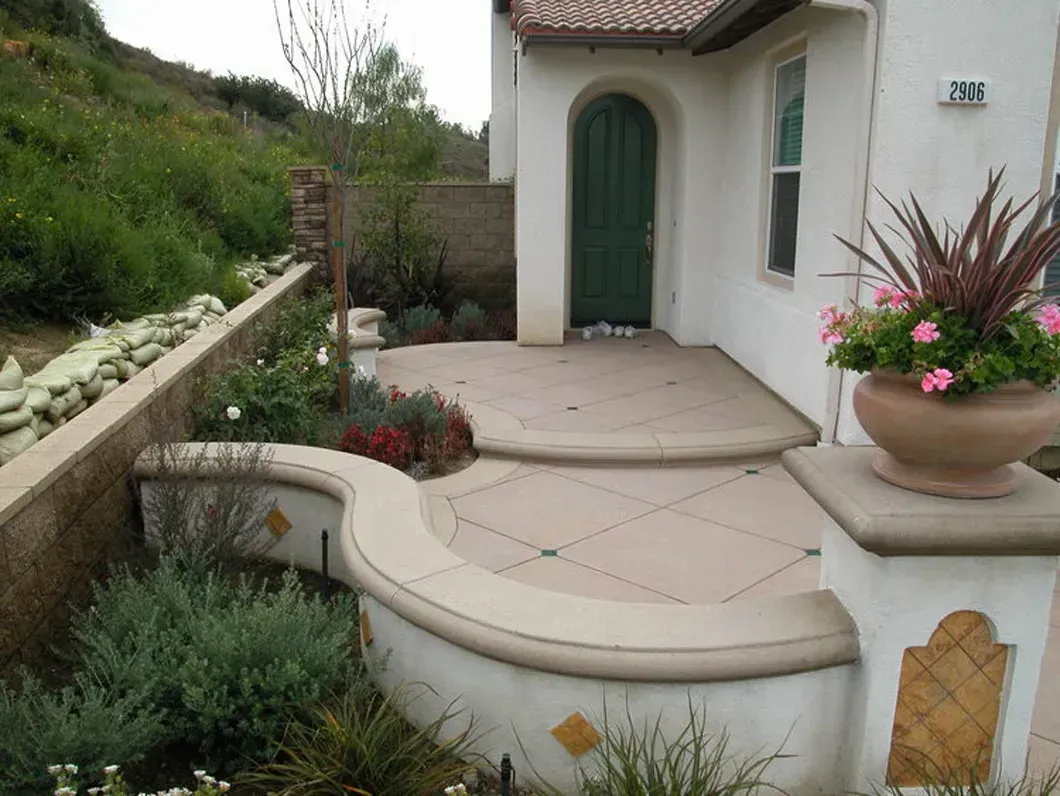 Curved beige concrete patio with steps, flower pot, and green door.