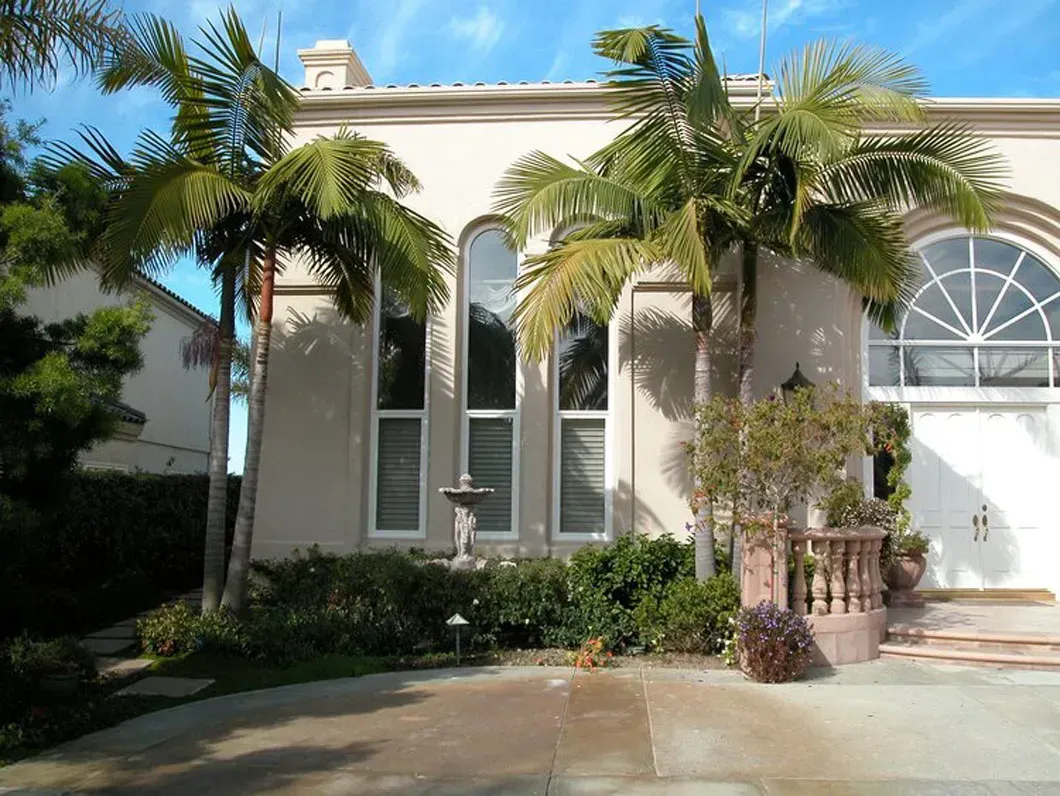 Beige stucco house with palm trees, tall windows, and a fountain.