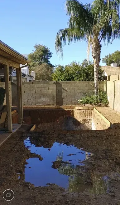 Backyard with a large puddle, palm tree, and a partially built structure.
