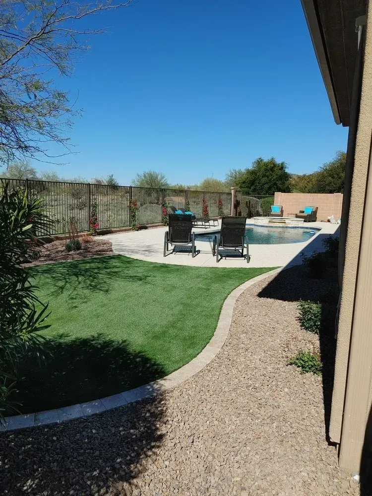 Backyard with pool, lounge chairs, green lawn, gravel path, and blue sky.