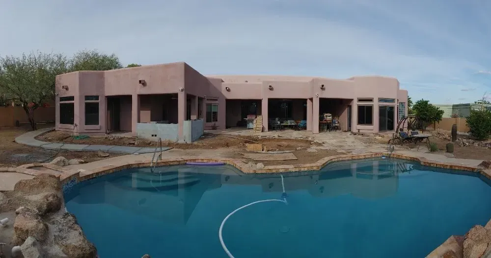 Backyard with a pool in front of a pink stucco house. The sky is blue.