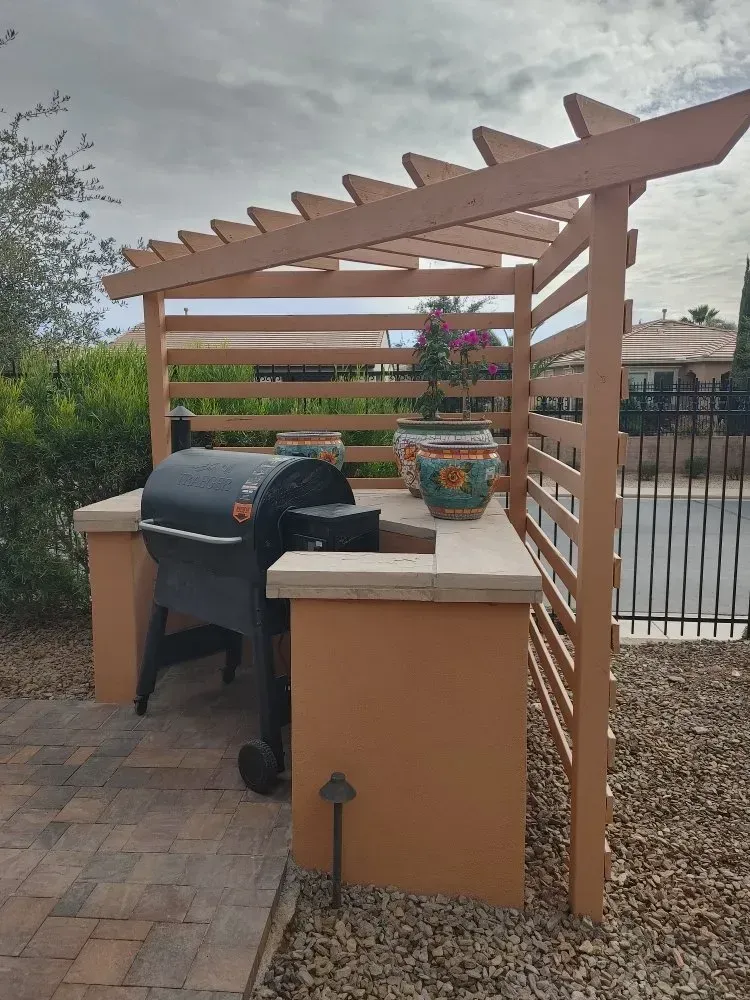 Outdoor grilling station with built-in counter, grill, pergola, and decorative pots, on brick patio.