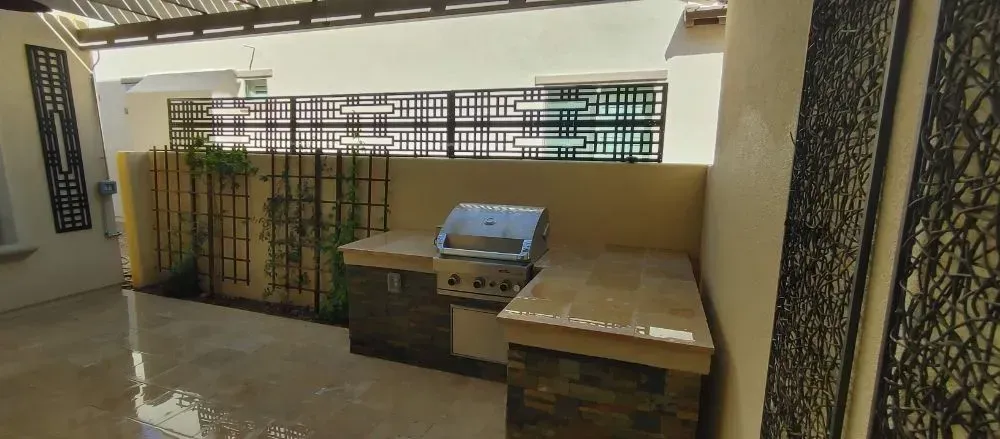 Outdoor built-in grill area with a stainless steel grill, stone countertops, and decorative metal screens.