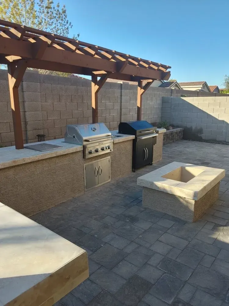 Outdoor kitchen with grill, pergola, and fire pit on a paver patio.