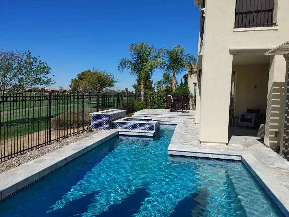 Backyard with a blue pool, a patio with a table and chairs, and a fire pit, all next to a two-story beige house.