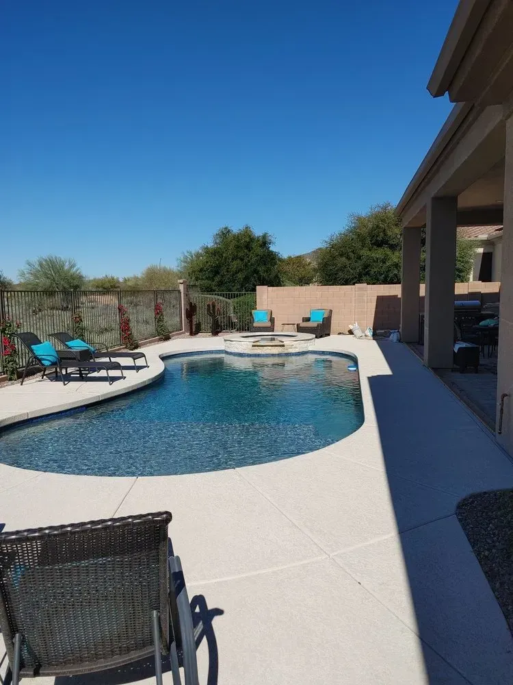 Swimming pool with lounge chairs, blue water, and patio area under a bright, sunny sky.