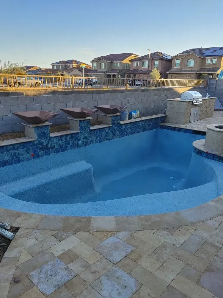 Newly constructed swimming pool with blue tile and stone patio. Backyard setting with houses in the background.