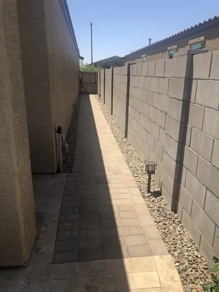 Narrow paved walkway between two walls, one cinder block, one stucco.