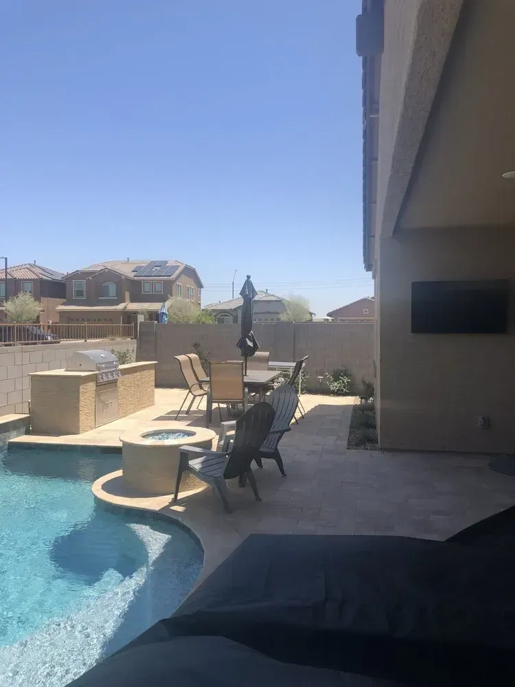 Backyard with pool, patio furniture, grill, and outdoor TV against a light-colored wall, sunny day.