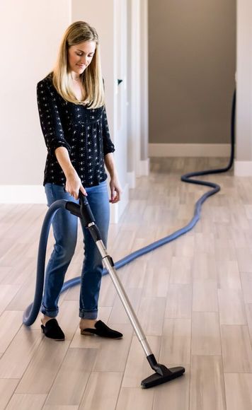 A woman is using a vacuum cleaner on a wooden floor.