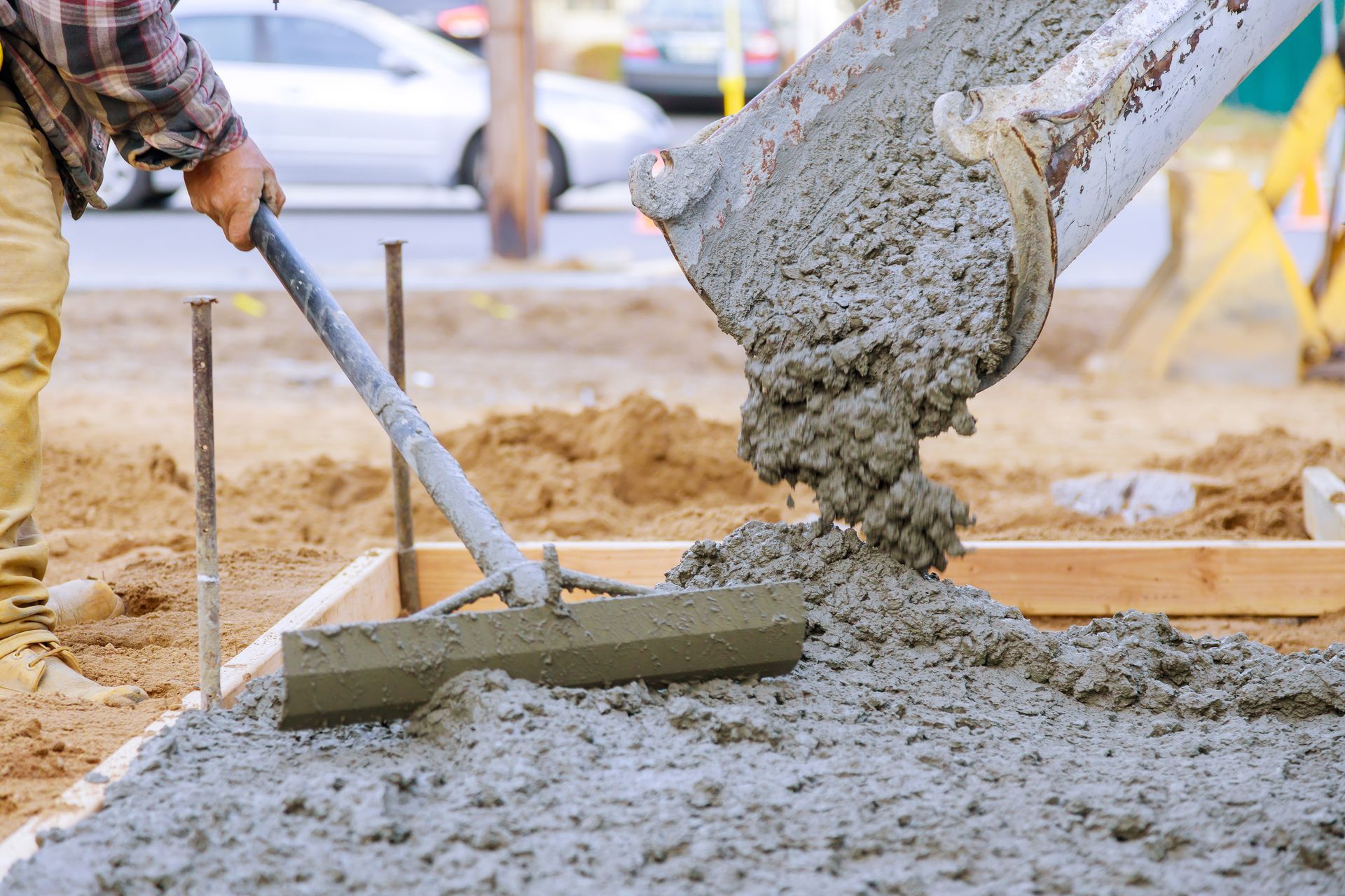 A man is using a rake to spread concrete on a construction site.