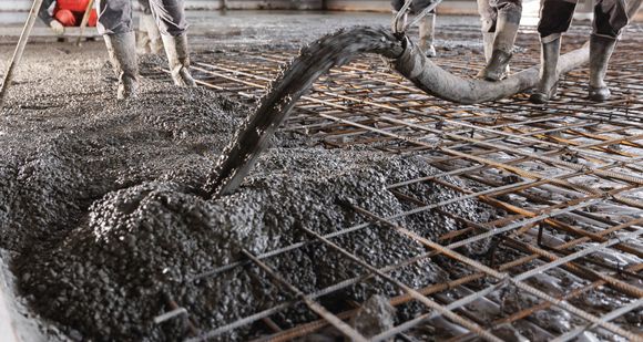 A group of construction workers are pouring concrete into a grid.