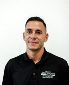 A man wearing a black polo shirt is smiling for the camera.