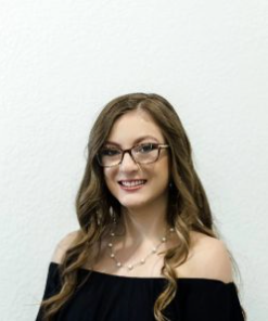 A woman wearing glasses and a black off the shoulder top is smiling.