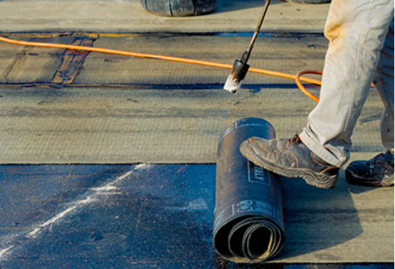 A person is rolling a roll of roofing material on a roof.