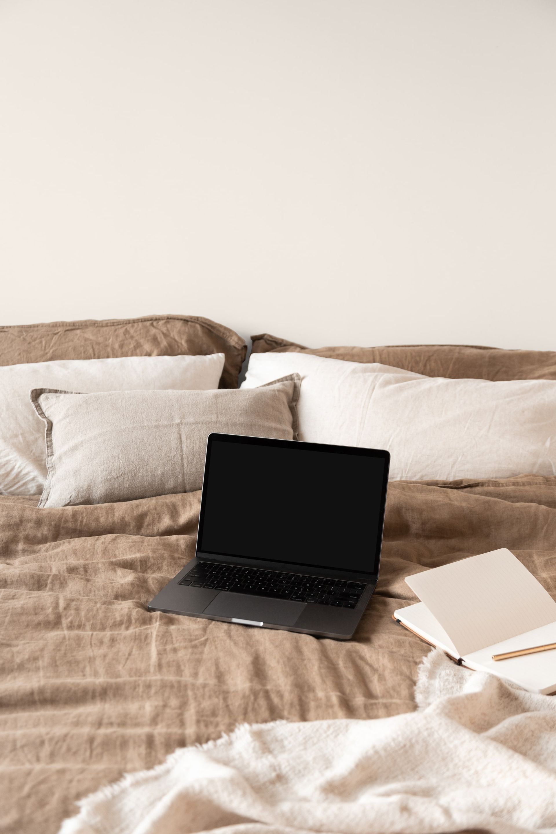 A laptop computer on a bed with notebook nearby.