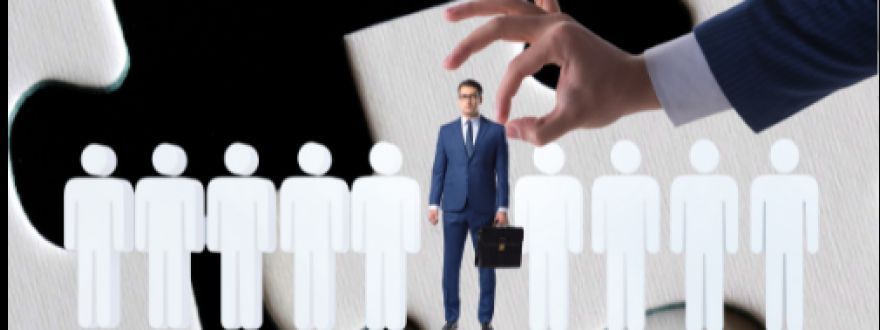 A large hand selects a professional in a suit from a row of paper cut-out figures against a puzzle piece background.