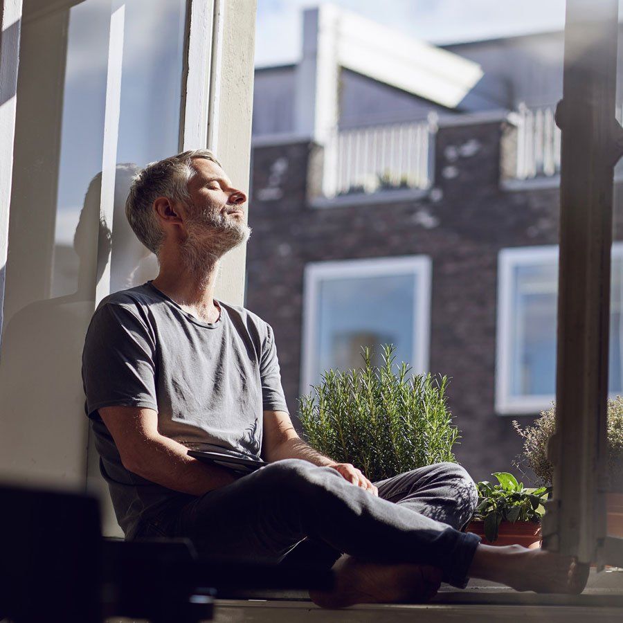 Mature man sitting at the window at home with closed eyes